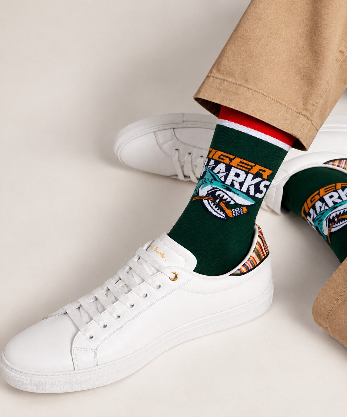 Dark green dress sock with a knit-in Tiger Sharks logo, worn with a white leather sneaker and khaki trousers