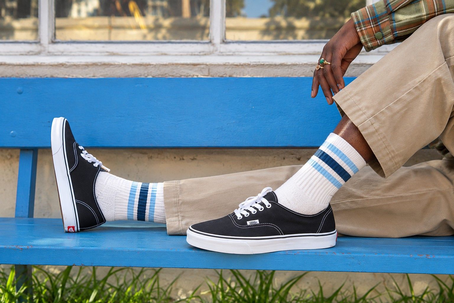 White cotton crew socks with light and dark blue stripes worn with black canvas sneakers on a blue bench