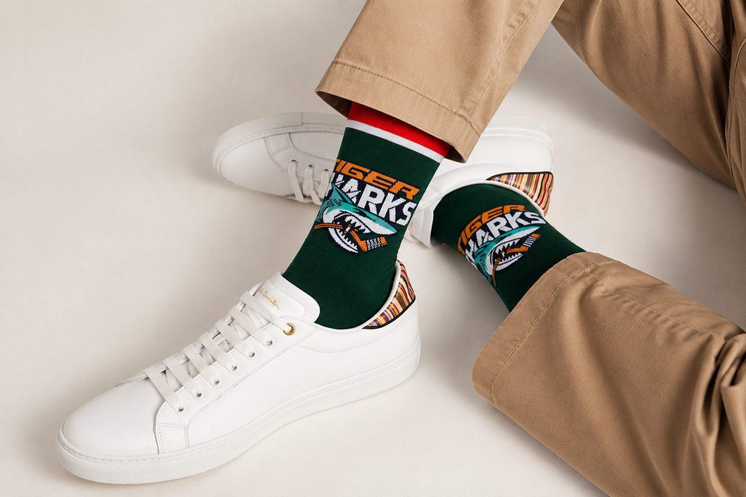 Dark green dress socks with a knit-in Tiger Sharks hockey logo, worn with white leather sneakers and khaki trousers
