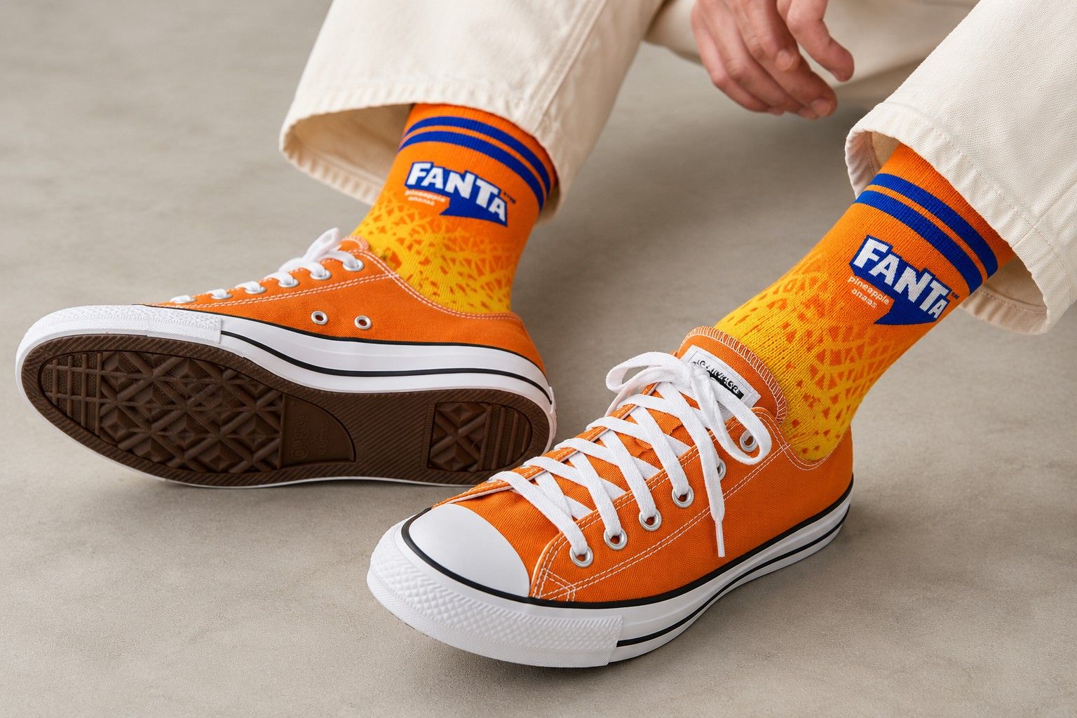 Orange and yellow Fanta sublimation print socks with blue stripes, worn with orange canvas sneakers and cream trousers